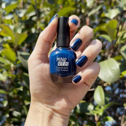 Hand with nails painted in MineVital Indigo, holding the bottle